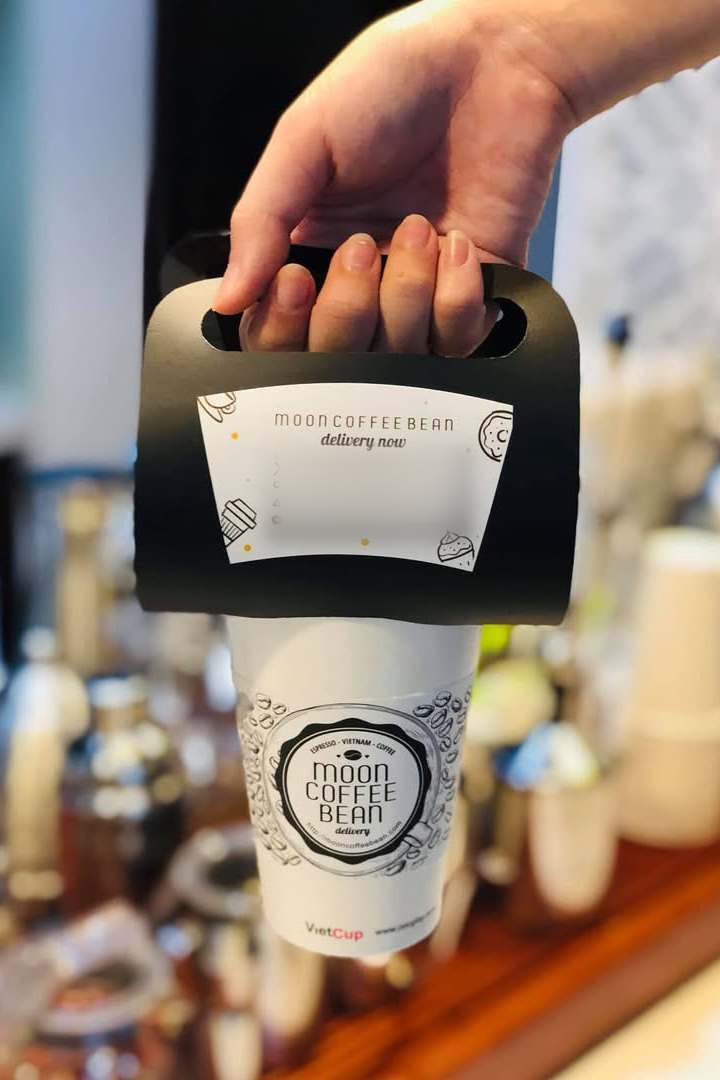 Quai xách giấy · Cách gọi lại nằm ngay trên tay khách Quai xách giấy đen Moon Coffee Bean kẹp trên miệng ly mang đi